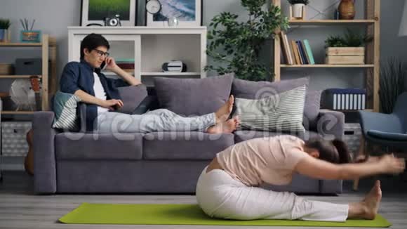 家庭主妇做瑜伽时丈夫用手提电脑工作用手机说话视频的预览图