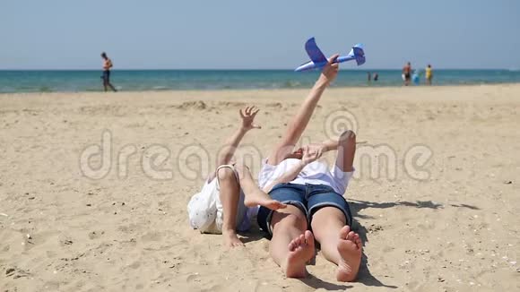 女人和一个孩子躺在沙滩上背景是大海一位母亲和一个小男孩正在玩飞机视频的预览图