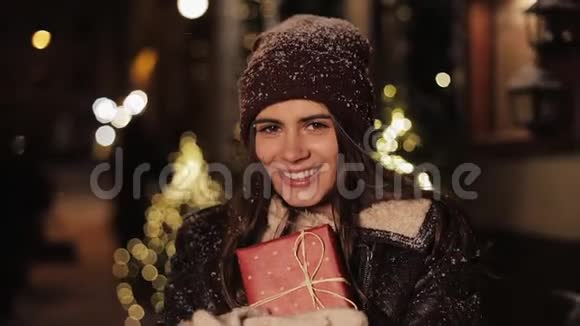 年轻漂亮女孩的肖像看上去很快乐拿着礼品盒和微笑站在落雪的户外视频的预览图