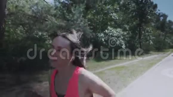 穿着粉红色衬衫在森林里奔跑的迷人的运动女孩苗条的女人有训练有素的身体做运动戴耳机的女孩是不是视频的预览图