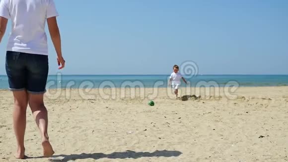 一位年轻的母亲和她的孩子正在沙滩上打球幸福的家庭正在踢足球的概念视频的预览图