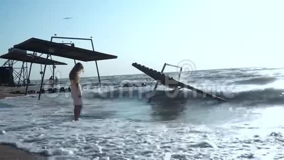 美丽的女孩低着头站在大海的波涛中站在海滩上靠近亭子视频的预览图