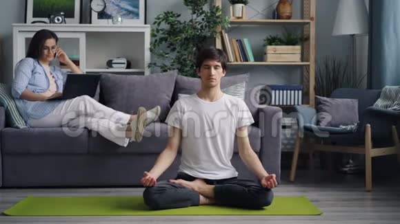当男朋友在瑜伽垫上冥想时女孩用手提电脑在手机上说话视频的预览图