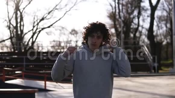一个长着深色卷发的英俊年轻人的肖像穿着灰色连帽衫的少年在春游公园里散步视频的预览图