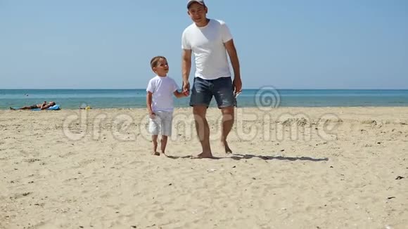 父子俩沿着海边沙滩朝镜头走去视频的预览图