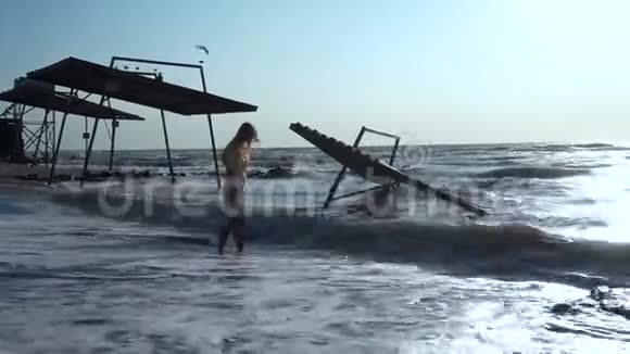 美丽的女孩低着头站在大海的波涛中站在海滩上靠近亭子视频的预览图