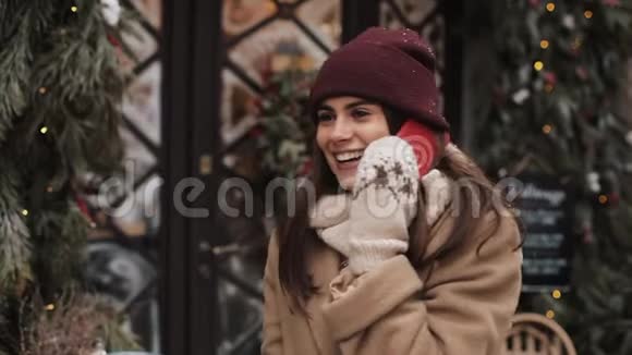 戴着冬帽和手套的年轻微笑迷人的女人站在外面在电话里笑着说视频的预览图