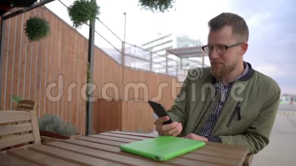 成年男子正在咖啡馆的露天平台休息通过智能手机视频通话视频的预览图