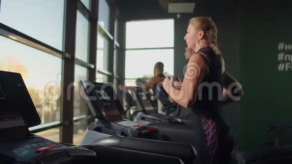 一位年轻漂亮的女士和三个人在健身房的跑步机上进行有氧运动室内视频的预览图