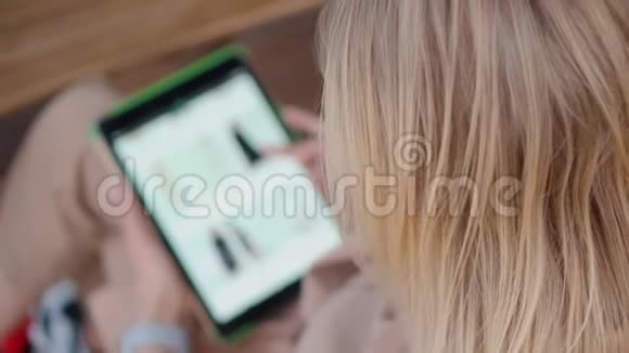 金发女郎正在用平板电脑检查网上时髦服装店的目录视频的预览图