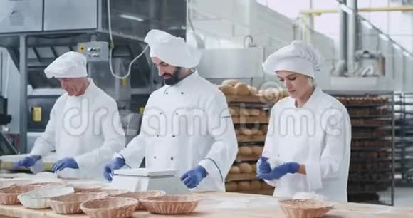 有魅力的女人面包师和她的同事面包师在一个烘焙行业快速工作形成面团过程视频的预览图