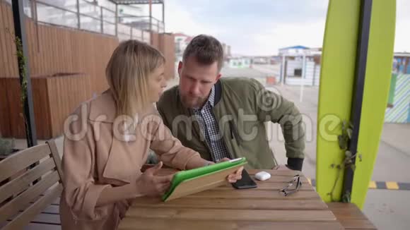 男人和女人正在看户外咖啡馆里的平板电脑视频的预览图