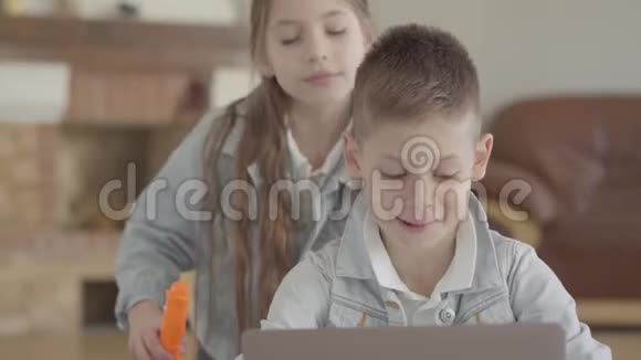 肖像可爱的小男孩坐在笔记本电脑上小女孩他的孪生妹妹在家里吹肥皂泡视频的预览图