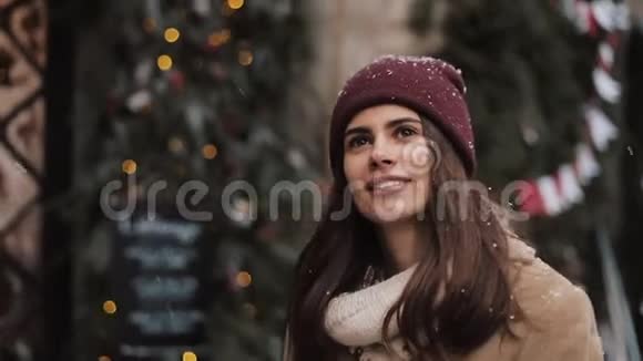 接近年轻的白种人漂亮的女孩戴着冬帽走路一个女人仰头看一场大雪在圣诞节落下视频的预览图