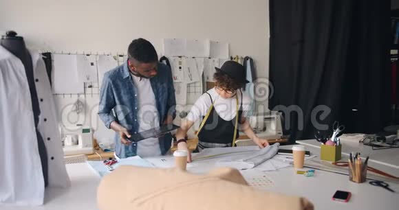 女孩和男人时装设计师在工作室里测量纺织品和使用平板电脑视频的预览图