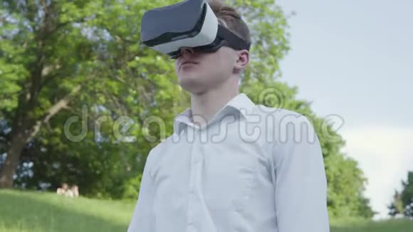 年轻人戴着虚拟现实耳机在公园里走来走去欣赏着真实的形象视频的预览图