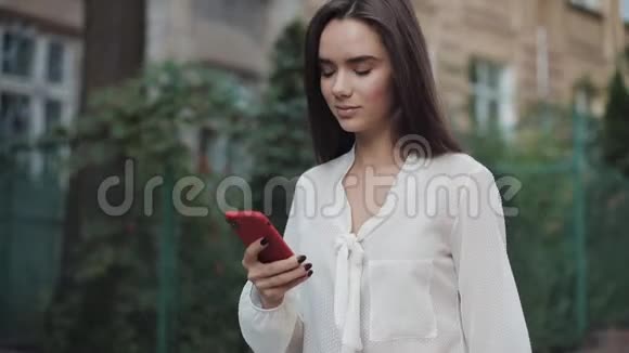 美丽的微笑的布鲁恩女孩走在舒适的老城街同时使用她的电话环顾四周视频的预览图