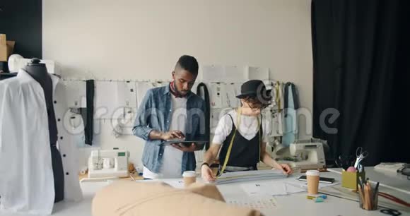 创意服装设计师在工作室中使用平板电脑和测量带设计服装视频的预览图