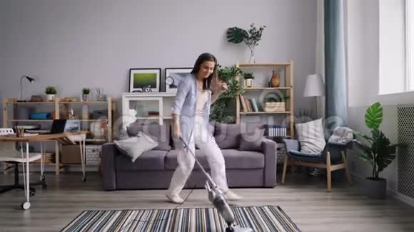 有魅力的年轻女士在家里跳舞听音乐吸尘地板视频的预览图