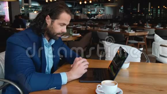 年轻的欧洲商人困乏坐在咖啡馆的一张桌子旁喝着一杯咖啡和一台笔记本电脑抑郁视频的预览图