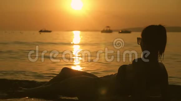 日落时分美丽的年轻女孩躺在海滩上度假的女孩在海滩上放松看日落夏季视频的预览图