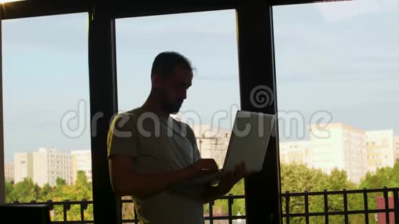 一个人站在窗户附近用手提电脑工作的剪影视频的预览图