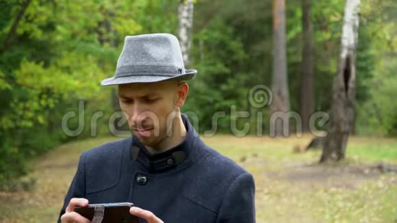 雨中戴着帽子和外套的男人看着电话里的东西视频的预览图
