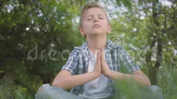 可爱的小帅哥坐在草地上沉思儿童练习瑜伽儿童的精神发展视频的预览图