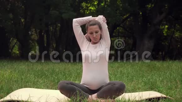 孕妇在公园的地毯上做瑜伽坐在莲花的位置做热身的手视频的预览图