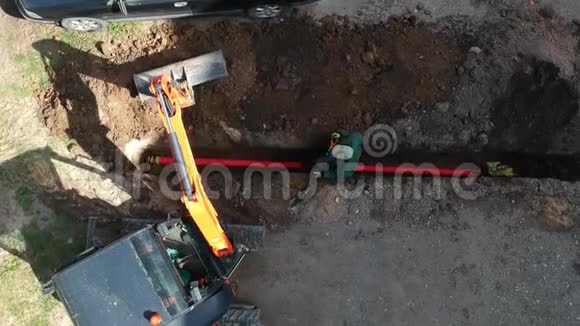 小型挖掘机和工人用管道空中掩埋城市街沟视频的预览图