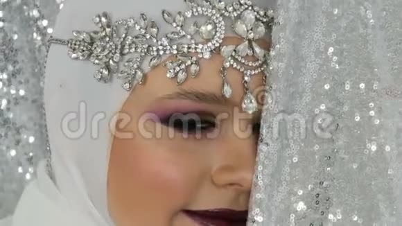 专业模特穿着白色的形象和银色的皇冠有一个明亮的多色化妆叫做烟熏眼摆姿势视频的预览图
