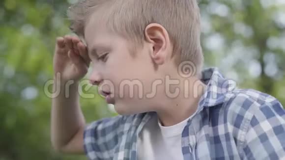 公园里一个穿格子衬衫的可爱英俊的男孩用手遮住太阳的眼睛视频的预览图