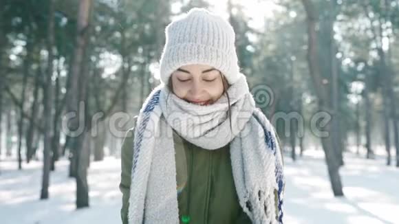 滑稽的微笑的女人戴着宽松的帽子和长长的温暖的围巾在阳光明媚的天气里把雪扔到镜头前雪地的冬天公园视频的预览图