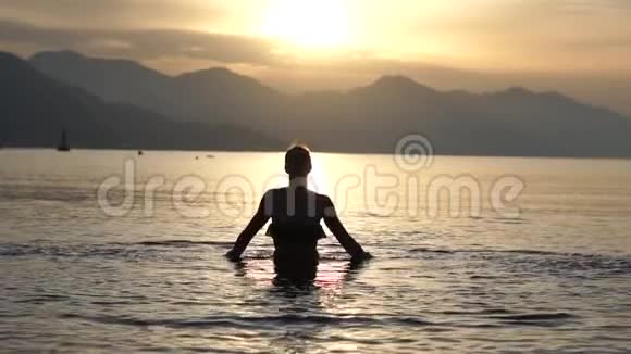 苗条的女孩在日出时以缓慢的动作在海里溅出美丽的水视频的预览图