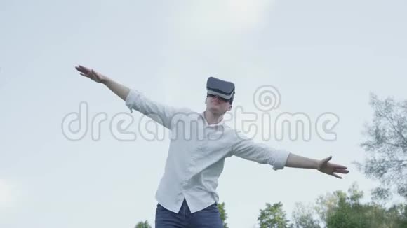 戴着虚拟现实耳机的人张开双臂模仿公园里飞机的飞行视频的预览图