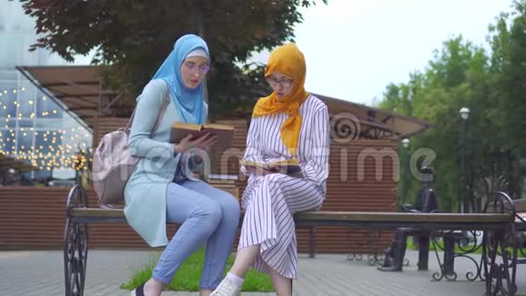 两名戴着传统围巾的穆斯林女学生手里拿着课本在公园里交流视频的预览图