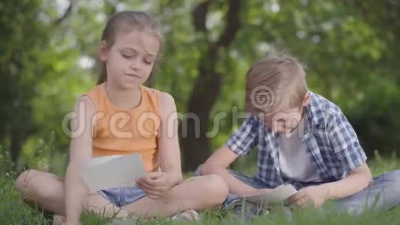 一幅可爱的英俊男孩穿着格子衬衫一个长发女孩看着公园里的一张纸的画像视频的预览图