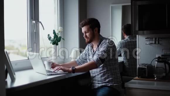 在厨房的窗户旁边打手提电脑的长胡子帅哥视频的预览图
