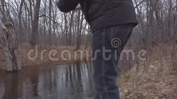 一个人在一个多云的秋日在一条小森林里的小河里用手机拍下了他的流水视频的预览图