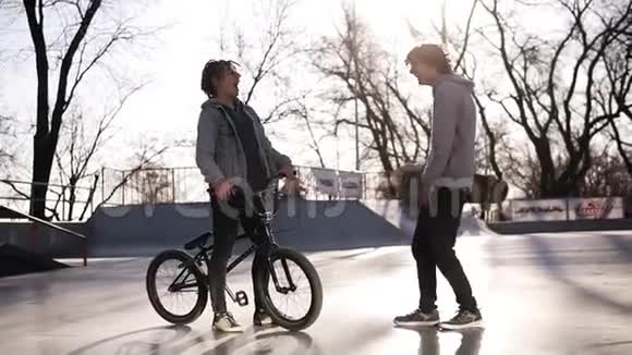 两个活跃的家伙朋友滑板车和BMX骑手在户外相遇在城市滑板公园朋友们在交流中视频的预览图
