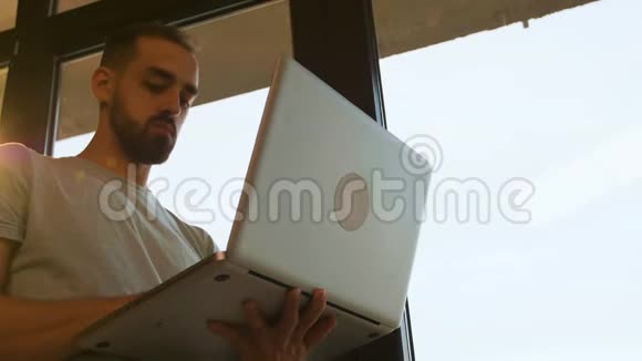 在靠近窗户的笔记本电脑上工作的经理的低角度镜头视频的预览图