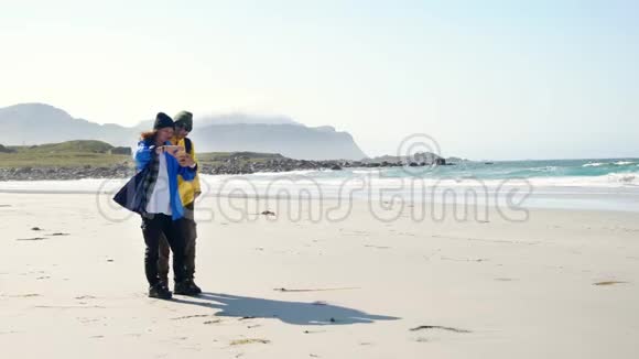 两位年轻的女游客正在海滩上用智能手机自拍视频的预览图