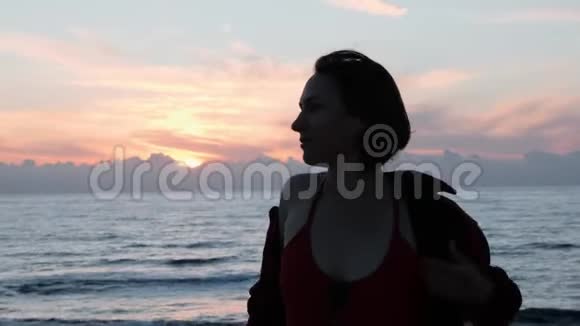 白种人年轻的女孩穿着红色衬衫对抗大海和日落迷人的黑发女人在黄昏时对海摆姿势可爱的女孩视频的预览图