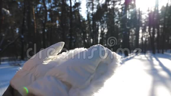 一个戴着白色手套的不可辨认的女人从她的手掌上吹下了雪站在冬林中的少女视频的预览图