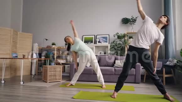 可爱的已婚夫妇女孩和男人在家训练在室内垫上瑜伽视频的预览图