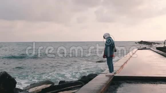 雨中站在码头的孤独少女寂寞的女孩看着暴风雨的大海女人站在荒芜的长廊上悲伤美丽视频的预览图