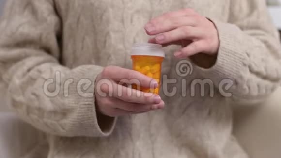 一个女人打开一罐药把一片药丸倒进她的手掌视频的预览图