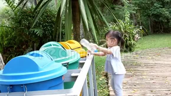小亚洲女孩把空塑料瓶扔进公园里的回收垃圾桶视频的预览图