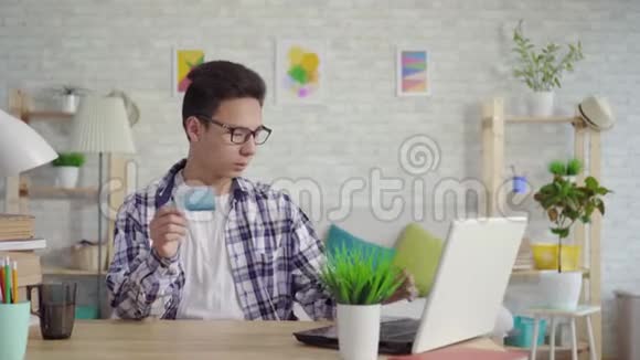 沮丧的亚洲年轻人穿着衬衫在笔记本电脑上用银行卡输入数据视频的预览图