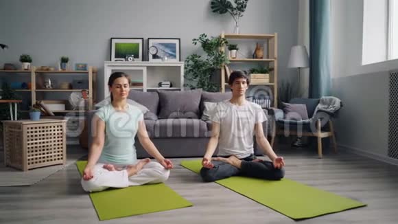 年轻人和女士在莲花的位置放松在家里的地板上冥想视频的预览图